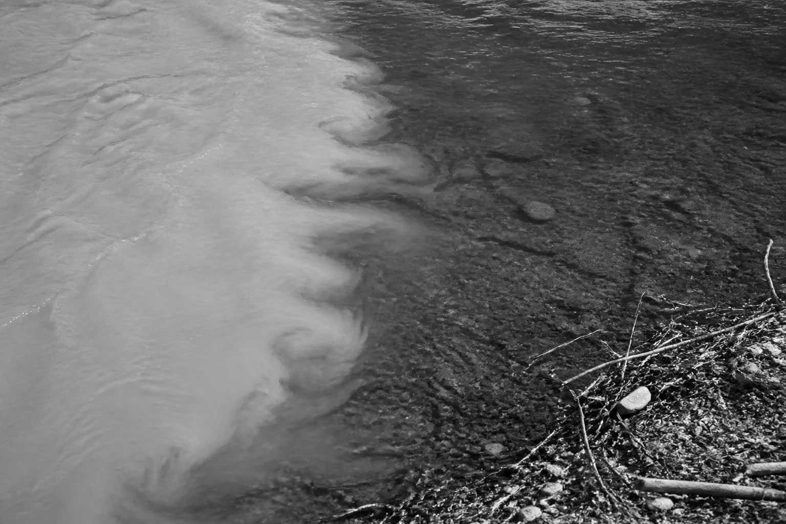Black-and-white silted water meeting clearer water at a rocky bank
