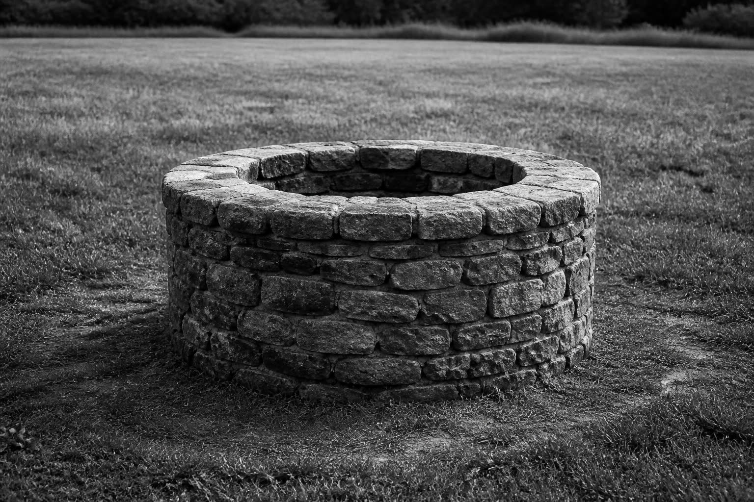 Black-and-white stone well standing alone in a grassy field
