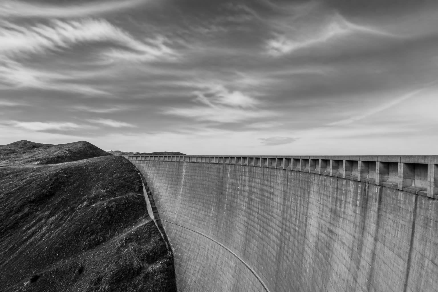 Black-and-white concrete dam wall under a wide sky