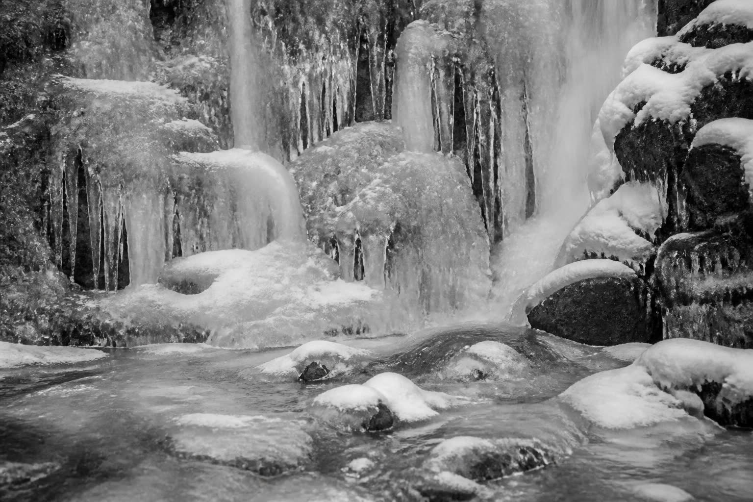 Black-and-white frozen waterfall and ice on a rocky stream
